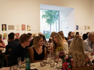 A group of people sat along trestle tables in a gallery space