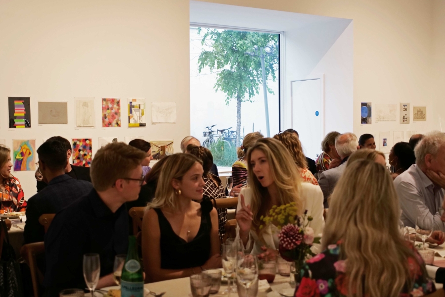 A group of people sat along trestle tables in a gallery space